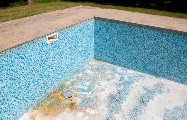 Empty swimming pool with dirty blue tiles and visible cracks