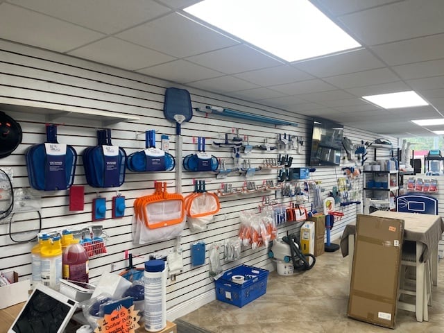 Retail store display wall with blue work gloves, safety vests, orange traffic cones, and various hardware supplies organized on white pegboard